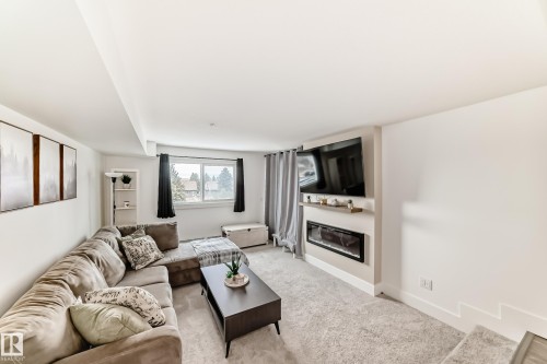 The living area features a built-in electric fireplace with a floating mantel, light-colored carpeting, and a window providing natural light - 307 9504 182 Street Nw, Edmonton, AB - Indoor Photo Showing Living Room With Fireplace