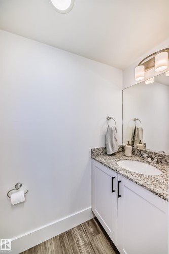 This powder room features a vanity with white cabinetry, a granite countertop, and a white basin - 307 9504 182 Street Nw, Edmonton, AB - Indoor Photo Showing Bathroom