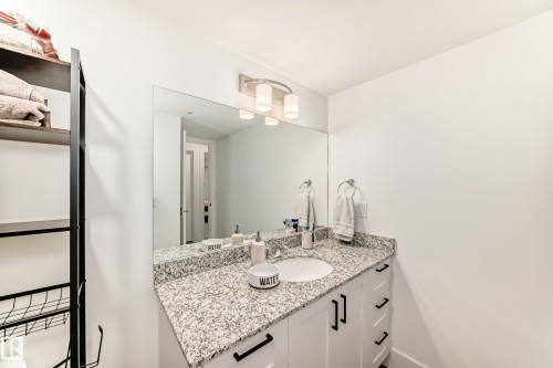 Bathroom vanity featuring a speckled granite countertop, an undermount sink, and white cabinetry with black hardware - 307 9504 182 Street Nw, Edmonton, AB - Indoor Photo Showing Bathroom