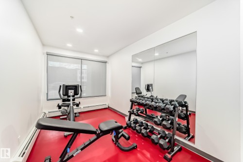 The fitness area features a bright red floor, a full wall mirror, and modern exercise equipment, including an exercise bike and a weight rack - 307 9504 182 Street Nw, Edmonton, AB - Indoor