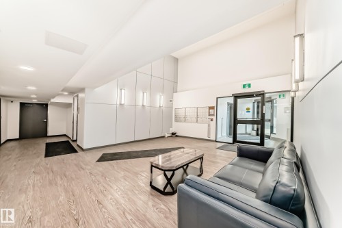 Lobby area featuring light wood-style flooring, a dark leather sofa, and modern wall lighting fixtures - 307 9504 182 Street Nw, Edmonton, AB - Indoor Photo Showing Other Room