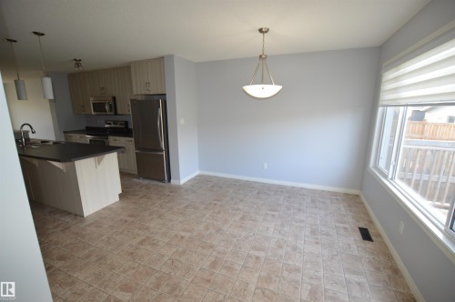Open-concept kitchen and dining area featuring light wood-finish cabinetry, stainless steel appliances, a dark countertop island with an integrated sink, and large windows providing abundant ambient light - 4310 Prowse Link Link, Edmonton, AB - Indoor Photo Showing Kitchen