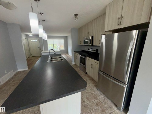 Kitchen featuring a spacious island with a double basin sink, dark countertops, and pendant lighting - 4310 Prowse Link Link, Edmonton, AB - Indoor Photo Showing Kitchen With Double Sink