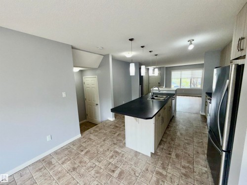 Kitchen featuring an island with a stainless steel sink and dark countertop, stainless steel refrigerator, light wood-finish cabinetry, and patterned tile flooring - 4310 Prowse Link Link, Edmonton, AB - Indoor Photo Showing Kitchen