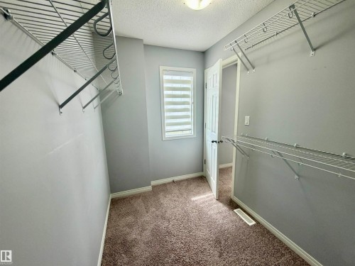 Spacious walk-in closet featuring wire shelving, wire hanging rods, neutral gray walls, brown carpet flooring, and a window with blinds - 4310 Prowse Link Link, Edmonton, AB - Indoor