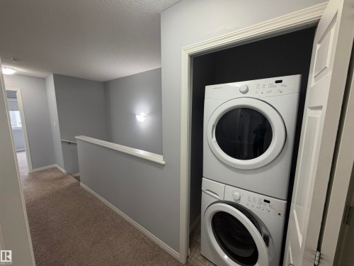 Dedicated laundry closet featuring a stacked washer and dryer, neutral gray wall tones, and crown molding - 4310 Prowse Link Link, Edmonton, AB - Indoor Photo Showing Laundry Room
