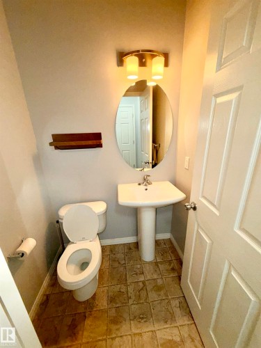 Powder room featuring a pedestal sink, oval mirror, and a wall-mounted light fixture with cylindrical shades - 4310 Prowse Link Link, Edmonton, AB - Indoor Photo Showing Bathroom