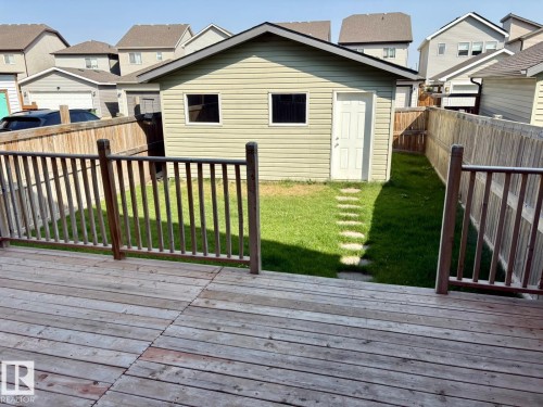 Expansive backyard featuring a detached accessory building with vinyl siding and a side entry door, a wooden privacy fence, a stepping stone pathway, and a wooden deck with railing - 4310 Prowse Link Link, Edmonton, AB - Outdoor With Deck Patio Veranda With Exterior