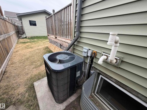 Exterior view featuring an air conditioning unit on a concrete pad, light green horizontal siding, and a basement window with a galvanized metal window well - 4310 Prowse Link Link, Edmonton, AB - Outdoor With Deck Patio Veranda With Exterior