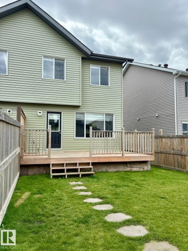 Rear exterior featuring light green siding, black door, multiple windows, and a wood deck with railings and steps - 4310 Prowse Link Link, Edmonton, AB - Outdoor With Deck Patio Veranda With Exterior