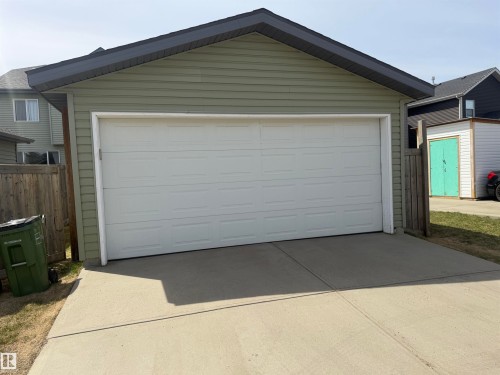 Detached garage featuring light green siding, a dark shingle roof, and a white panel garage door - 4310 Prowse Link Link, Edmonton, AB - Outdoor With Exterior