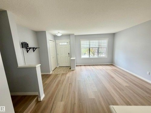 Open concept living area featuring wood-finish flooring, a contemporary ceiling light fixture, a front entry door with transom windows, and a large window with horizontal blinds - 4310 Prowse Link Link, Edmonton, AB - Indoor Photo Showing Other Room