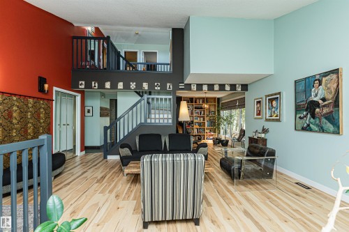 Open-concept living area featuring light wood-finish flooring, a multi-level layout with a balcony overlook, a built-in staircase with painted railings, and a wall of built-in shelving - 1235 104 Street, Edmonton, AB - Indoor Photo Showing Other Room