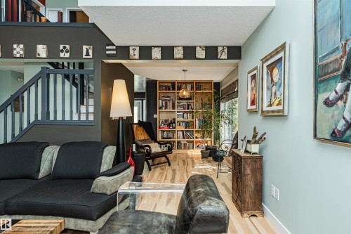 Expansive living area with wood-finish flooring, a built-in bookshelf, a staircase with dark railings, a light blue wall, and a recessed ceiling - 1235 104 Street, Edmonton, AB - Indoor