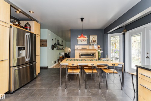 Spacious kitchen and dining area featuring a stainless steel refrigerator, light wood-finish cabinetry, dark tile flooring, and double patio doors with decorative glass inserts - 1235 104 Street, Edmonton, AB - Indoor Photo Showing Other Room