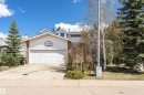 Front exterior featuring a white siding and brick facade, an attached two-car garage, mature evergreen trees, a concrete driveway, and a partially visible upper-level dormer - 1235 104 Street, Edmonton, AB  - Outdoor 