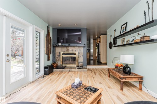 Living area featuring wood-finish flooring, a stone-tiled fireplace with a brass insert, and recessed ceiling lighting - 1235 104 Street, Edmonton, AB - Indoor With Fireplace