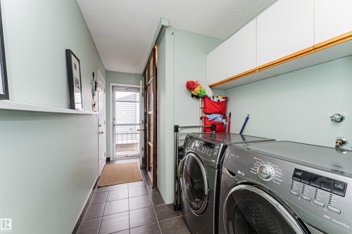 Dedicated laundry area featuring modern appliances, wall-mounted cabinetry, a built-in shelf, and tile flooring - 1235 104 Street, Edmonton, AB - Indoor Photo Showing Laundry Room