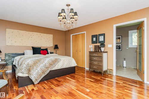 Spacious bedroom featuring wood-finish flooring, a built-in closet with double doors, and a decorative chandelier - 1235 104 Street, Edmonton, AB - Indoor Photo Showing Bedroom