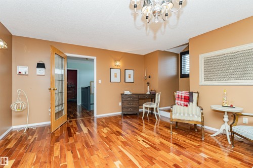 Spacious interior room featuring rich wood-finish flooring, a contemporary chandelier, a window with horizontal blinds, and a glass-paneled interior door - 1235 104 Street, Edmonton, AB - Indoor Photo Showing Other Room