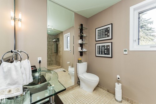 Bathroom featuring a glass vessel sink, mounted mirror with vanity lighting, a walk-in shower with tiled walls and pebble flooring, and a window with white trim - 1235 104 Street, Edmonton, AB - Indoor Photo Showing Bathroom