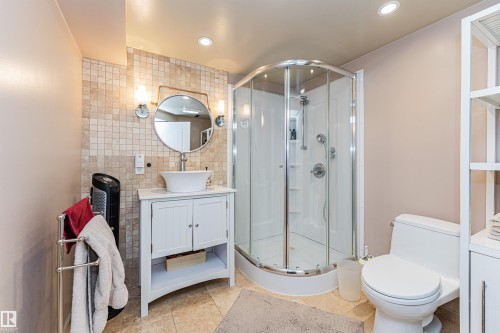 Full bathroom featuring a corner glass-enclosed shower, white vanity with vessel sink, round wall mirror with sconce lighting, and tiled flooring - 1235 104 Street, Edmonton, AB - Indoor Photo Showing Bathroom