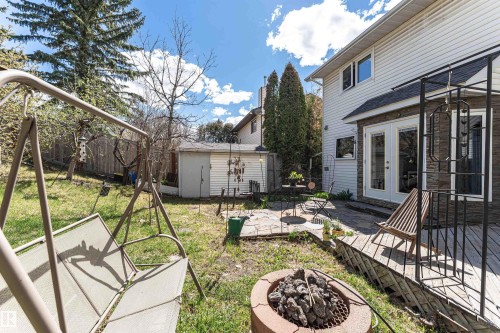 Expansive backyard featuring a stone patio, wooden deck, built-in fire pit, and mature trees - 1235 104 Street, Edmonton, AB - Outdoor