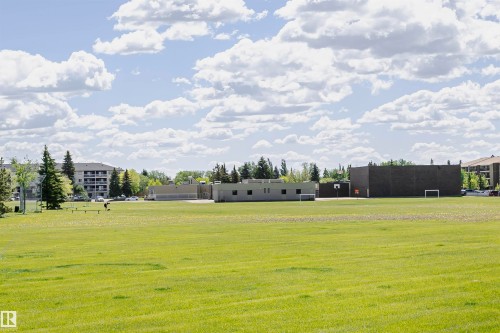 Expansive green space featuring large grass areas, visible evergreen trees, and a distant low-rise residential building - 1235 104 Street, Edmonton, AB - Outdoor With View