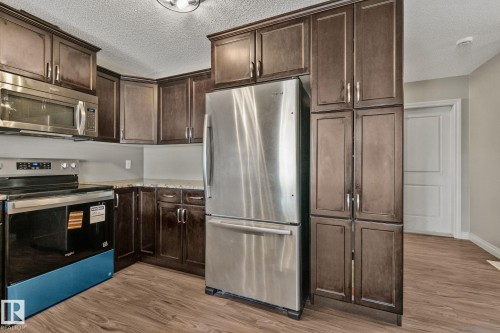Kitchen featuring rich wood-finish cabinetry, stainless steel appliances, speckled countertops, and wood-look flooring - 46 445 Brintnell Boulevard, Edmonton, AB - Indoor Photo Showing Kitchen With Stainless Steel Kitchen