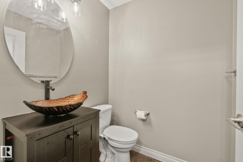 Powder room featuring a dark wood-finish vanity with a vessel sink and a wall-mounted faucet, complemented by an oval mirror and a three-light vanity fixture - 46 445 Brintnell Boulevard, Edmonton, AB - Indoor Photo Showing Bathroom