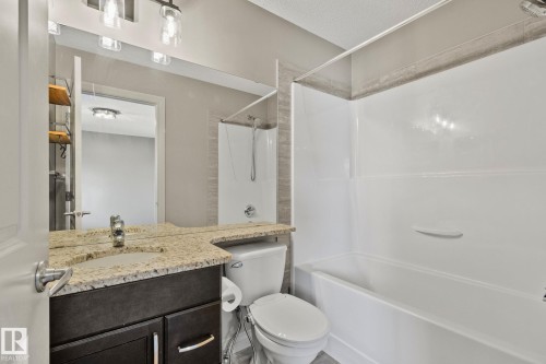Bathroom featuring a granite-finish countertop, dark wood-finish vanity with chrome hardware, an integrated sink, and a white tub and shower combination with a tiled surround - 46 445 Brintnell Boulevard, Edmonton, AB - Indoor Photo Showing Bathroom