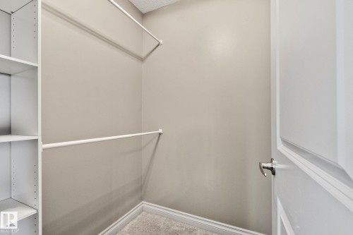 Walk-in closet featuring built-in shelving, dual hanging rods, light gray wall paint, white trim, and gray carpeting - 46 445 Brintnell Boulevard, Edmonton, AB - Indoor