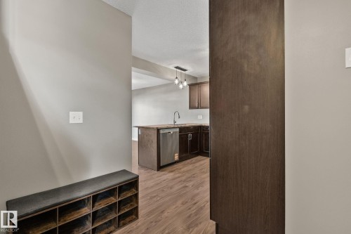 Open concept kitchen with wood-finish flooring, dark cabinetry, a kitchen island, stainless steel dishwasher, and a contemporary pendant light fixture - 46 445 Brintnell Boulevard, Edmonton, AB - Indoor