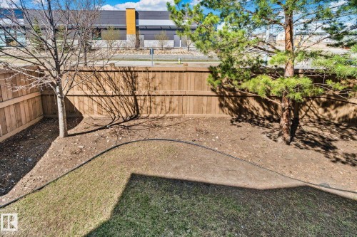 Fenced backyard area featuring a wood fence, partial grass coverage, and mature trees - 46 445 Brintnell Boulevard, Edmonton, AB - Outdoor