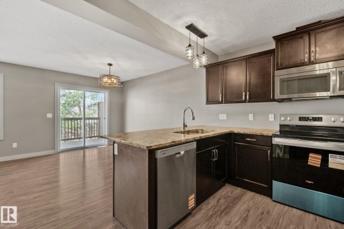 Kitchen island featuring a single-basin sink with a gooseneck faucet, dark wood cabinetry, and a light-colored countertop - 46 445 Brintnell Boulevard, Edmonton, AB - Indoor Photo Showing Kitchen With Stainless Steel Kitchen