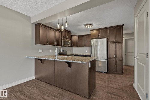 Kitchen featuring an island with stone-finish countertop, dark wood-finish cabinetry, stainless steel appliances, and wood-finish flooring - 46 445 Brintnell Boulevard, Edmonton, AB - Indoor Photo Showing Kitchen With Stainless Steel Kitchen