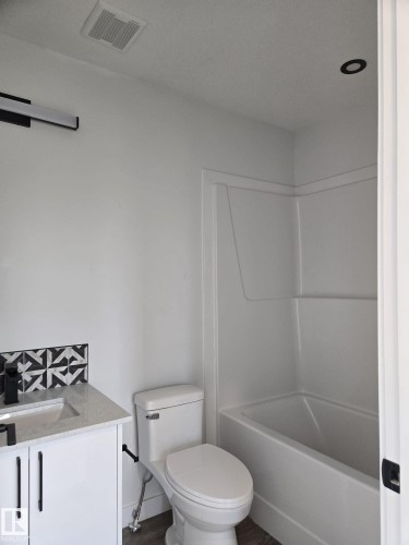 Bathroom featuring a white vanity with a light-colored countertop, black-and-white patterned tile backsplash, and a contemporary wall-mounted light fixture - 12440 47 Street, Edmonton, AB - Indoor Photo Showing Bathroom