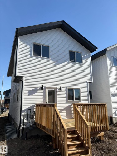 Rear exterior featuring a new construction wood deck, white horizontal siding, black gabled roof, and multiple windows with dark frames - 12440 47 Street, Edmonton, AB - Outdoor With Exterior