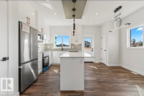 Modern kitchen featuring stainless steel appliances, white cabinetry, a patterned tile backsplash, a central island with a light-colored countertop, and recessed lighting - 12440 47 Street, Edmonton, AB - Indoor Photo Showing Kitchen With Upgraded Kitchen