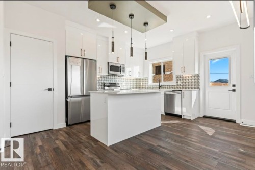 Modern kitchen featuring wood-finish flooring, white cabinetry, stainless steel appliances, a center island, and contemporary pendant lighting - 12440 47 Street, Edmonton, AB - Indoor Photo Showing Kitchen With Upgraded Kitchen