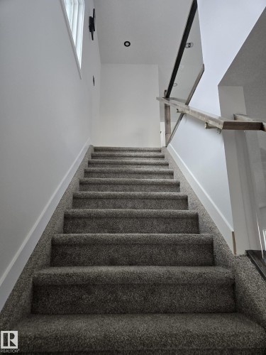 Carpeted staircase featuring a modern glass and wood-finish railing - 12440 47 Street, Edmonton, AB - Indoor Photo Showing Other Room