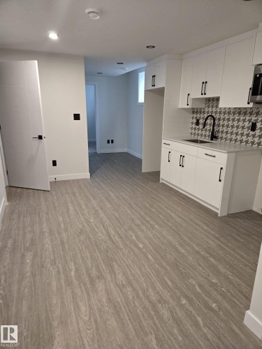 Full kitchen featuring white cabinetry with black hardware, houndstooth pattern tile backsplash, and a black faucet - 12440 47 Street, Edmonton, AB - Indoor