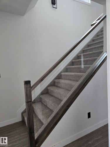 Contemporary staircase featuring gray carpeted steps, a dark wood-finish handrail, and clear glass panel balusters - 12440 47 Street, Edmonton, AB - Indoor Photo Showing Other Room