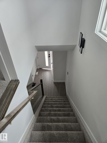 Carpeted staircase featuring a modern glass railing with a wood-finish handrail - 12440 47 Street, Edmonton, AB - Indoor Photo Showing Other Room