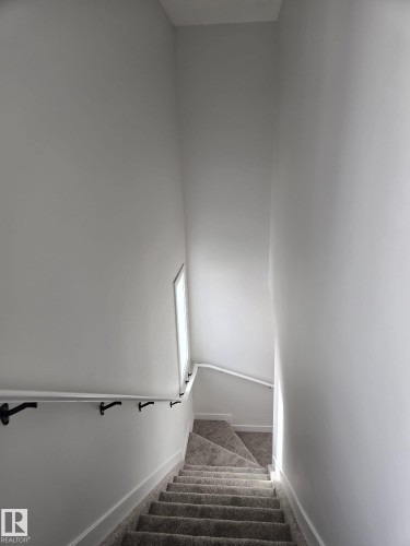 Stairwell featuring light gray carpeted steps, white walls, and a white handrail with black brackets - 12440 47 Street, Edmonton, AB - Indoor
