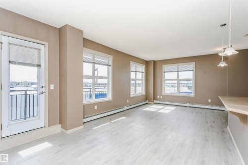 Open-concept living space with light wood-finish flooring, neutral wall tones, and multiple windows - 1-402 4245 139 Avenue, Edmonton, AB - Indoor Photo Showing Other Room