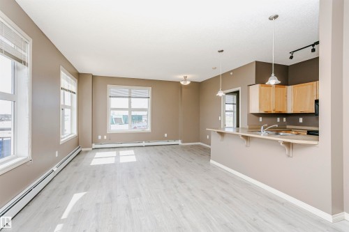 Open-concept living area featuring light wood-finish flooring, multiple large windows with blinds, and a kitchen island with pendant lighting - 1-402 4245 139 Avenue, Edmonton, AB - Indoor