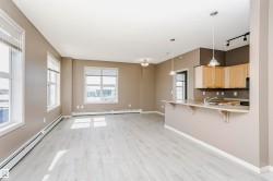 Open-concept living area featuring light wood-finish flooring, multiple large windows with blinds, and a kitchen island with pendant lighting - 