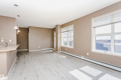 Open concept living area featuring light wood-finish flooring, neutral wall tones, and multiple large windows - 1-402 4245 139 Avenue, Edmonton, AB - Indoor