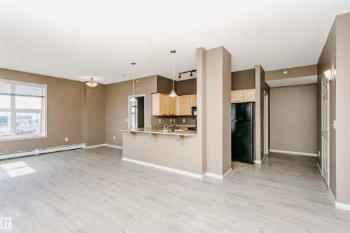 Open-concept living area with light wood-finish flooring, a kitchen peninsula with pendant lighting, and natural wood cabinetry - 1-402 4245 139 Avenue, Edmonton, AB - Indoor